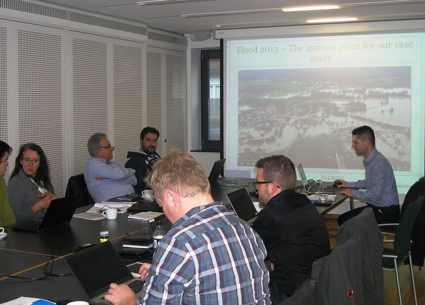 Frauen und Männer sitzen am Konferenztisch im SVB, während Projekte mit einer Powerpointpräsentation vorgestellt werden.