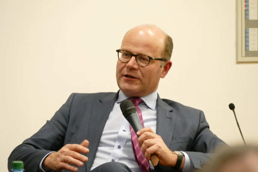 Europaminister Oliver Schenk in Nahaufnahme, er sitzt in einem Sessel auf dem Podium, in der linken Hand hält er ein Mikrofon, gestikuliert während er mit den Gesprächspartnern diskutiert