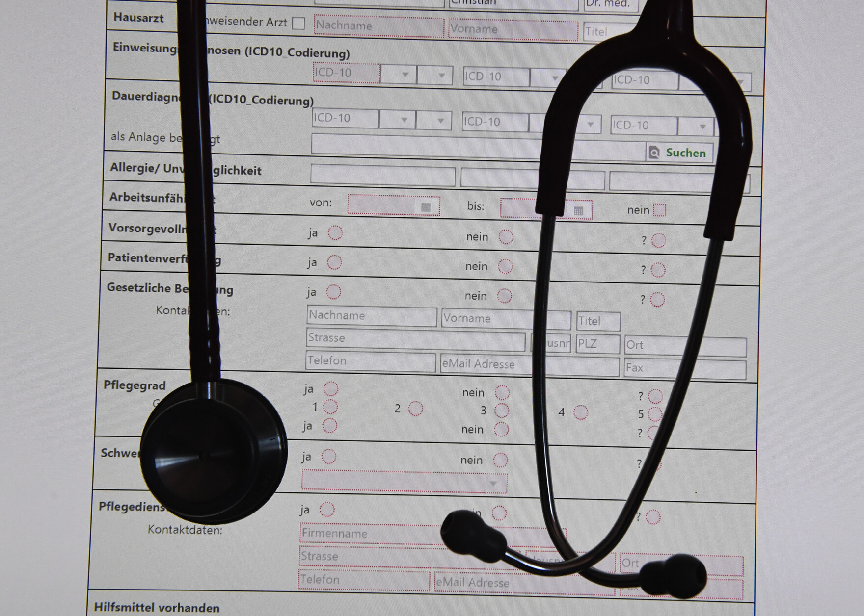 In einem Behandlungszimmer einer Praxis hängt ein Stethoskop vor einer auf einem Bildschirm dargestellten digitalen Patientenakte. 